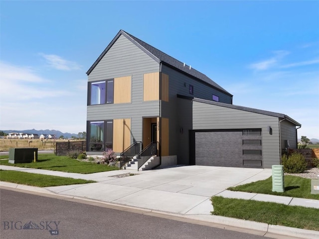 contemporary home with a mountain view, driveway, an attached garage, and a front yard