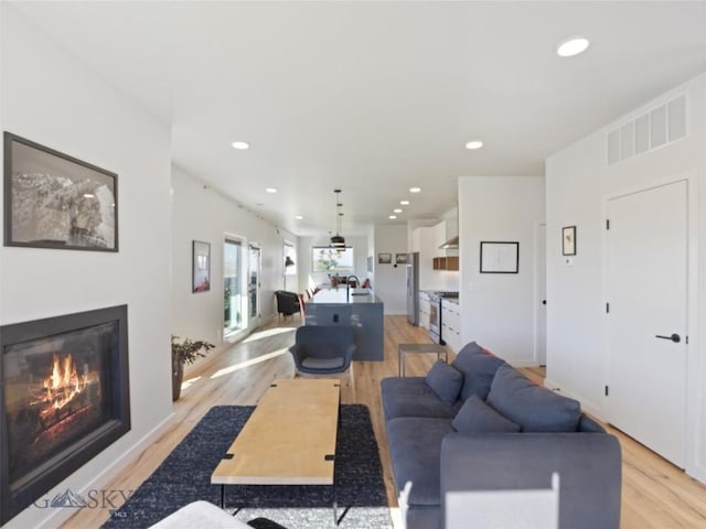 living area featuring light wood-type flooring, visible vents, recessed lighting, and a glass covered fireplace