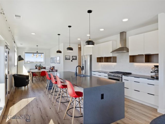 kitchen with dark countertops, modern cabinets, an island with sink, and wall chimney exhaust hood