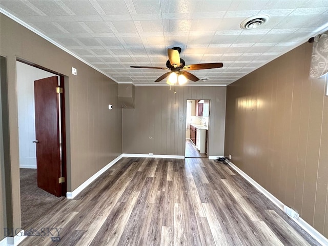 unfurnished room featuring hardwood / wood-style flooring, ceiling fan, ornamental molding, and wooden walls