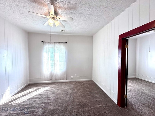 empty room with ceiling fan, dark carpet, and wooden walls