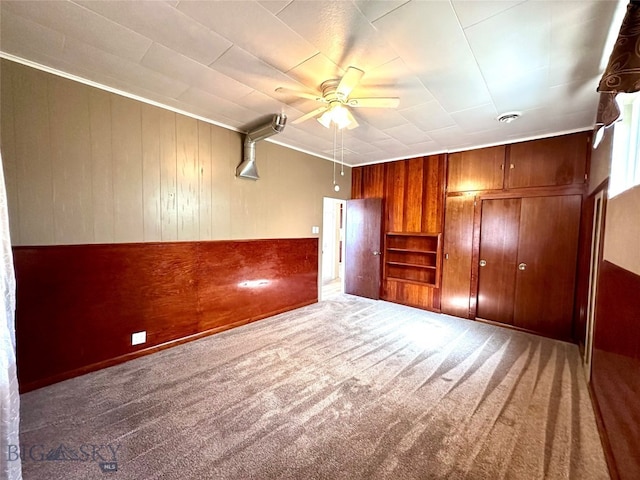 unfurnished bedroom with carpet, ornamental molding, ceiling fan, and wooden walls