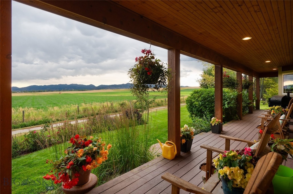 wooden terrace with a mountain view, a yard, a rural view, and covered porch