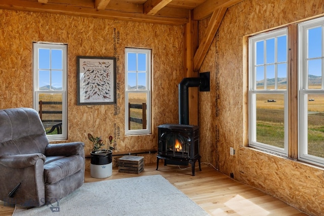 sitting room with light hardwood / wood-style floors, vaulted ceiling with beams, and a wood stove