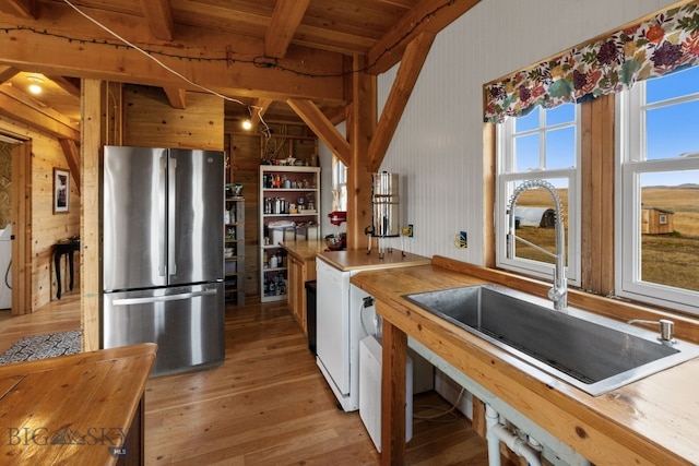 kitchen with wood walls, stainless steel refrigerator, sink, beamed ceiling, and light wood-type flooring