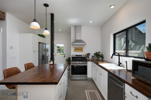 kitchen with sink, stainless steel appliances, wood counters, and wall chimney range hood