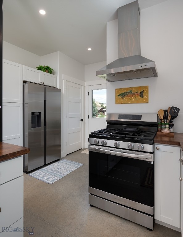 kitchen with appliances with stainless steel finishes, white cabinetry, wall chimney exhaust hood, and butcher block countertops