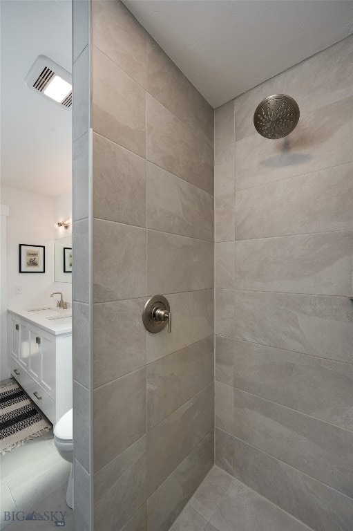 bathroom with tile patterned flooring, toilet, a tile shower, and vanity