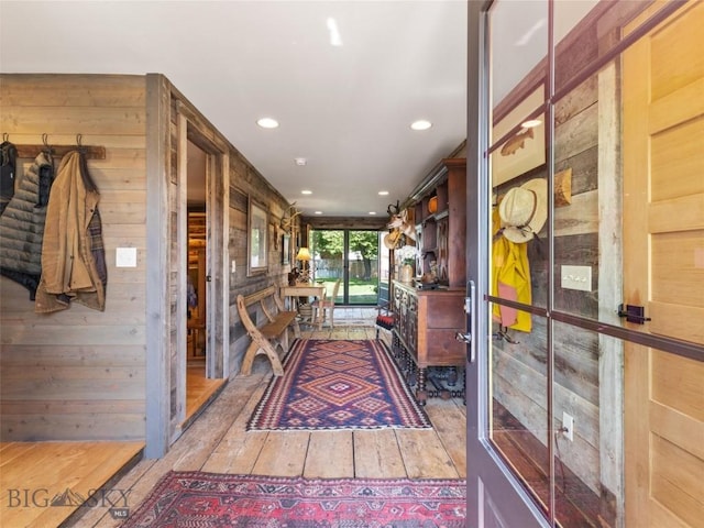 hallway with light wood-type flooring, wooden walls, and recessed lighting