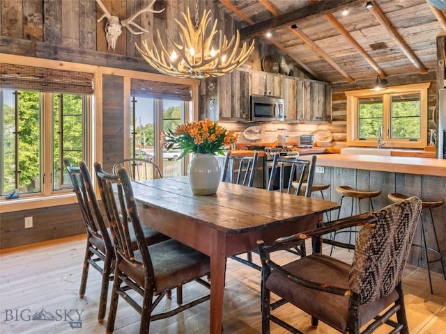 dining area with vaulted ceiling with beams, wooden ceiling, light wood-style flooring, a notable chandelier, and wooden walls