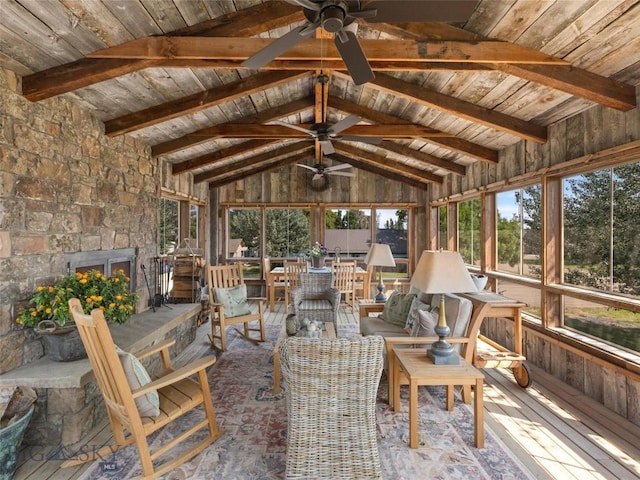 sunroom / solarium with vaulted ceiling with beams, ceiling fan, an outdoor stone fireplace, and wooden ceiling