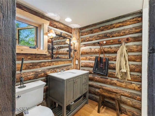 bathroom with rustic walls, vanity, toilet, and wood finished floors