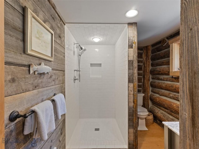 full bathroom featuring rustic walls, a tile shower, toilet, and wood finished floors