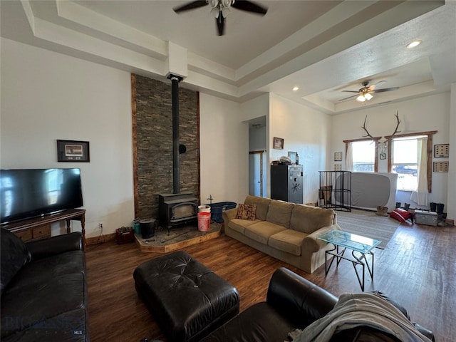 living room with hardwood / wood-style flooring, ceiling fan, a raised ceiling, and a wood stove