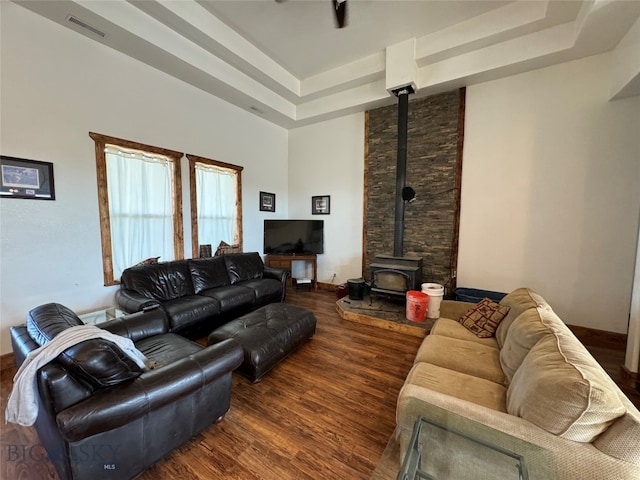 living room featuring a tray ceiling, a wood stove, and dark wood-type flooring