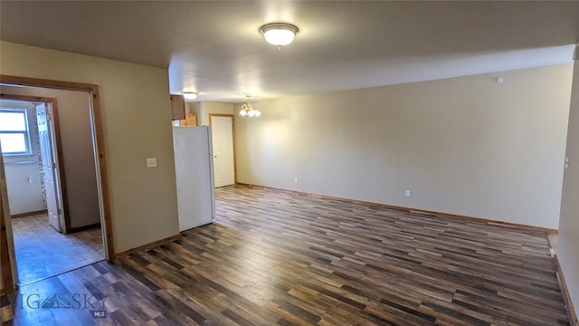 spare room with an inviting chandelier and dark hardwood / wood-style flooring