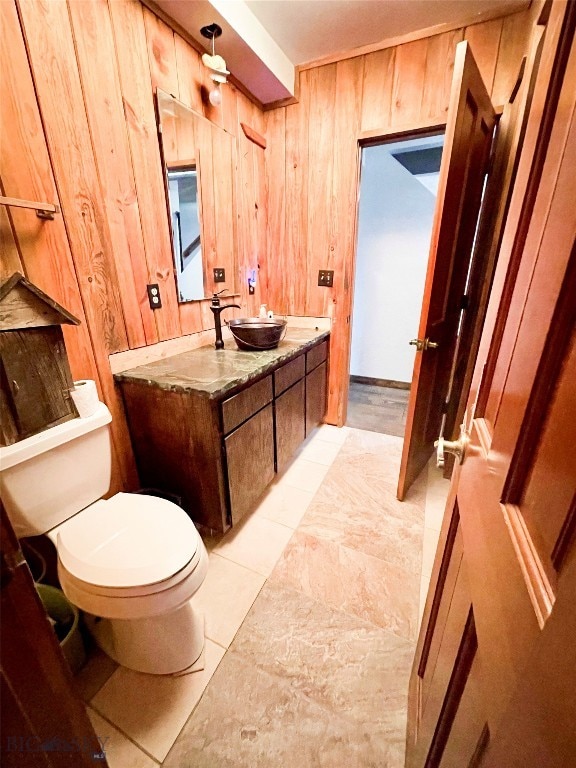 bathroom with vanity, toilet, wood walls, and tile patterned flooring