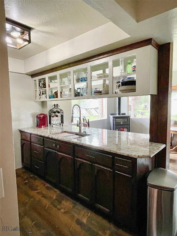 kitchen featuring light stone counters, sink, dark hardwood / wood-style floors, dark brown cabinetry, and a textured ceiling