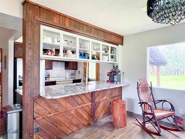 interior space featuring a textured ceiling, hardwood / wood-style floors, kitchen peninsula, sink, and light stone counters