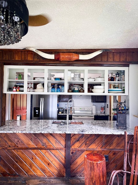 bar with a textured ceiling, stainless steel refrigerator with ice dispenser, stone countertops, sink, and electric stove