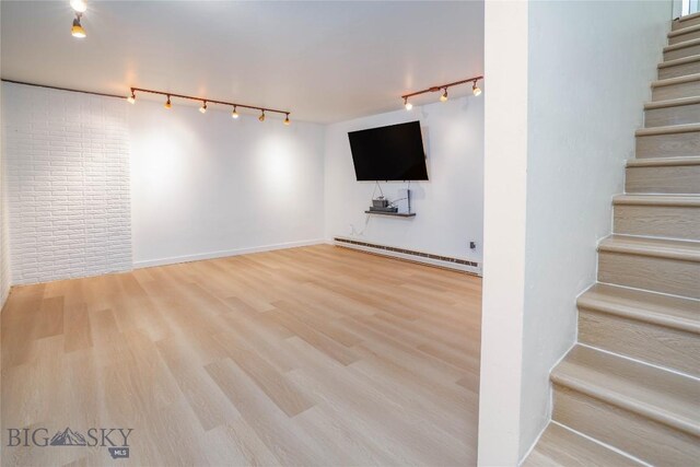 basement featuring wood-type flooring, track lighting, and a baseboard heating unit