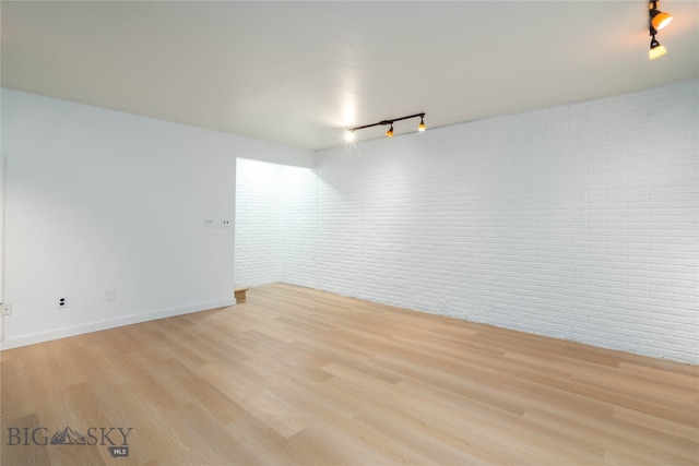 unfurnished room featuring light hardwood / wood-style floors, brick wall, and track lighting