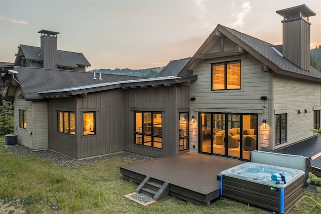 back house at dusk featuring a hot tub, central AC, and a wooden deck