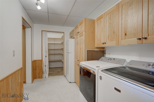 clothes washing area featuring washer and dryer, cabinets, light carpet, and wooden walls