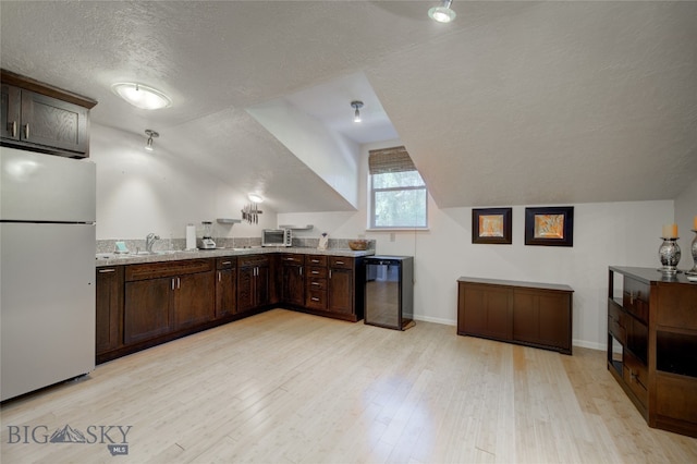 kitchen with a textured ceiling, lofted ceiling, light stone counters, white refrigerator, and light wood-type flooring