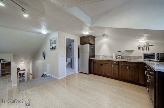 kitchen featuring a textured ceiling, vaulted ceiling, stainless steel fridge, light hardwood / wood-style floors, and light stone counters