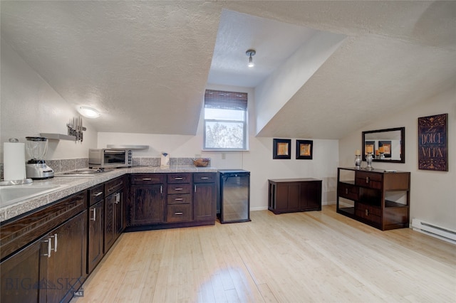 kitchen featuring light wood-type flooring, a textured ceiling, dark brown cabinets, baseboard heating, and lofted ceiling