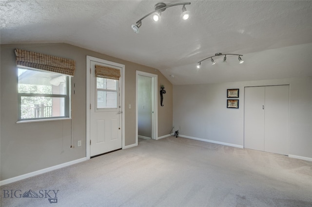 entryway with lofted ceiling, light colored carpet, rail lighting, and a textured ceiling