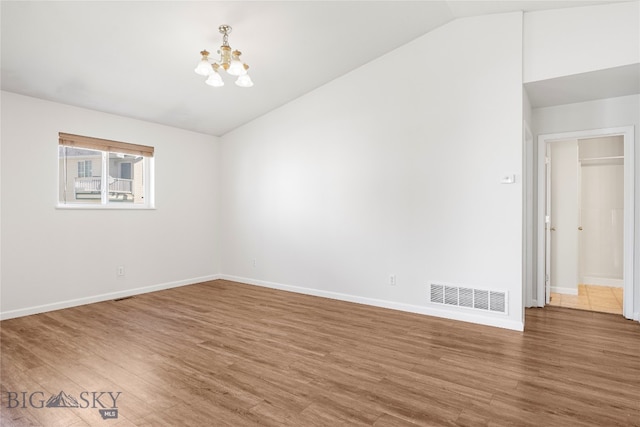 spare room with hardwood / wood-style flooring, an inviting chandelier, and vaulted ceiling