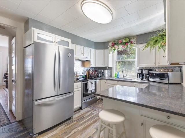 kitchen featuring a sink, light wood-type flooring, stainless steel appliances, white cabinets, and a peninsula