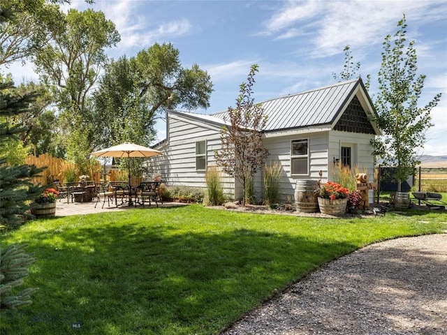 back of house featuring a standing seam roof, metal roof, fence, a yard, and a patio