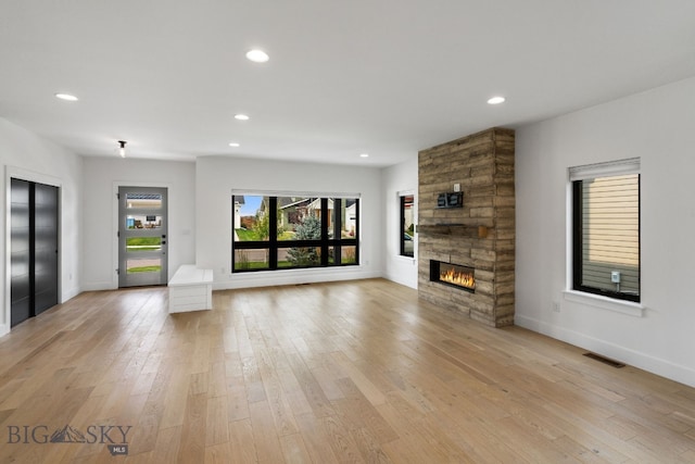 unfurnished living room with elevator, light wood-type flooring, and a stone fireplace