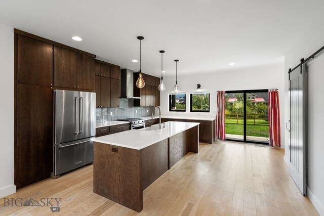 kitchen with a barn door, wall chimney exhaust hood, decorative light fixtures, tasteful backsplash, and premium appliances