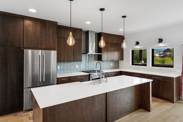 kitchen featuring wall chimney exhaust hood, premium appliances, decorative light fixtures, tasteful backsplash, and dark brown cabinetry