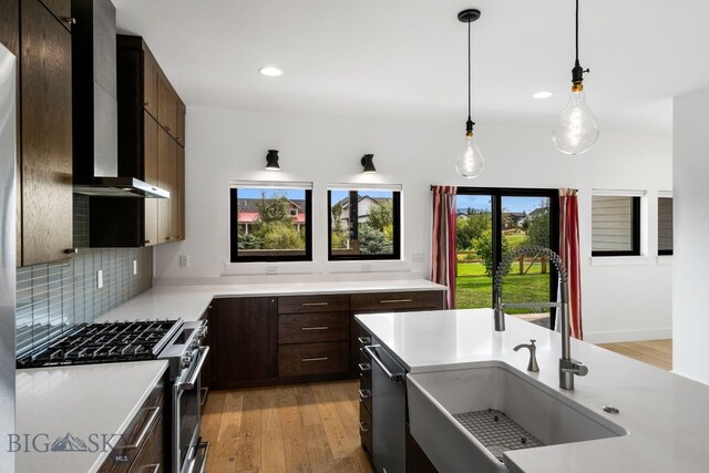 kitchen featuring light hardwood / wood-style floors, tasteful backsplash, wall chimney range hood, pendant lighting, and appliances with stainless steel finishes