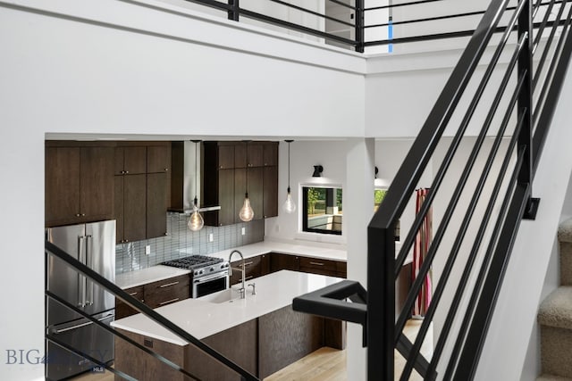 kitchen featuring sink, tasteful backsplash, dark brown cabinetry, wall chimney range hood, and premium appliances