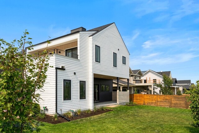 rear view of house featuring a balcony and a yard