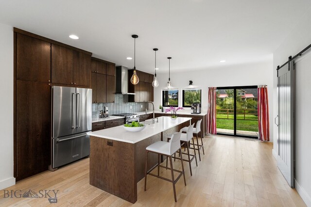 kitchen featuring a barn door, hanging light fixtures, wall chimney exhaust hood, backsplash, and premium appliances