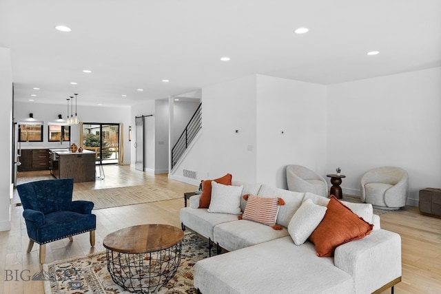 living area with light wood-type flooring, recessed lighting, a barn door, stairway, and baseboards