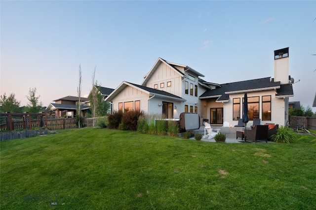 back house at dusk with an outdoor living space, a lawn, and a patio area