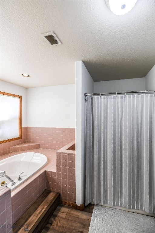 bathroom with a textured ceiling, independent shower and bath, and wood-type flooring