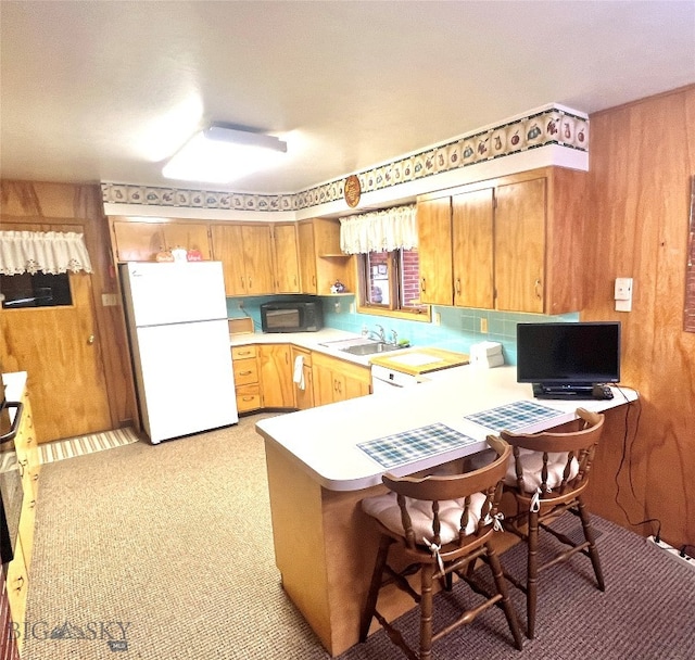 kitchen with a kitchen bar, kitchen peninsula, sink, light colored carpet, and white refrigerator