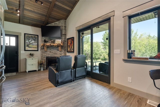 living room with lofted ceiling with beams, a stone fireplace, wood ceiling, and light hardwood / wood-style flooring