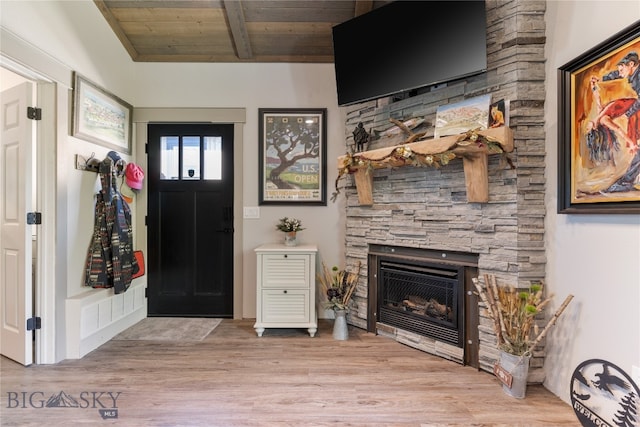 foyer entrance with vaulted ceiling with beams, a fireplace, wood ceiling, and light hardwood / wood-style flooring