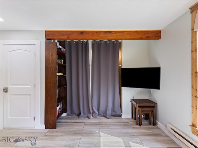 interior space featuring beamed ceiling, light hardwood / wood-style floors, and a baseboard heating unit