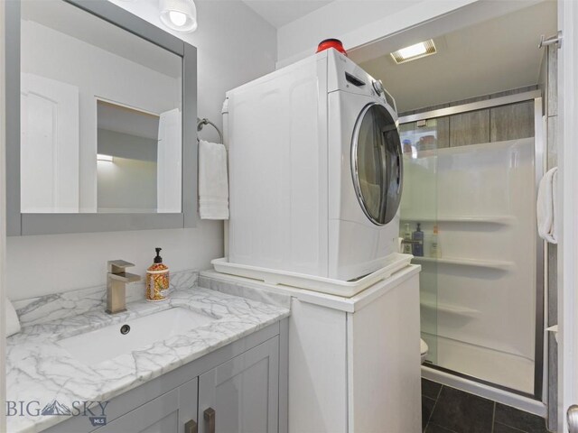 laundry area with sink, dark tile patterned floors, and stacked washer and clothes dryer